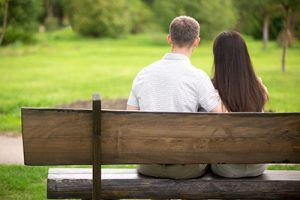 Jóvenes novios sentados en un banco de madera en el parque, vista posterior