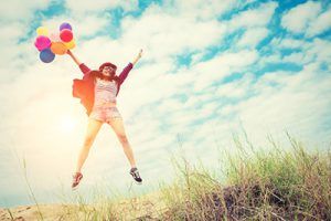 Mujer joven saltando feliz con globos en la playa